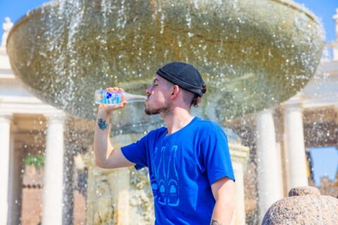 man chugging water bottle near a fountain